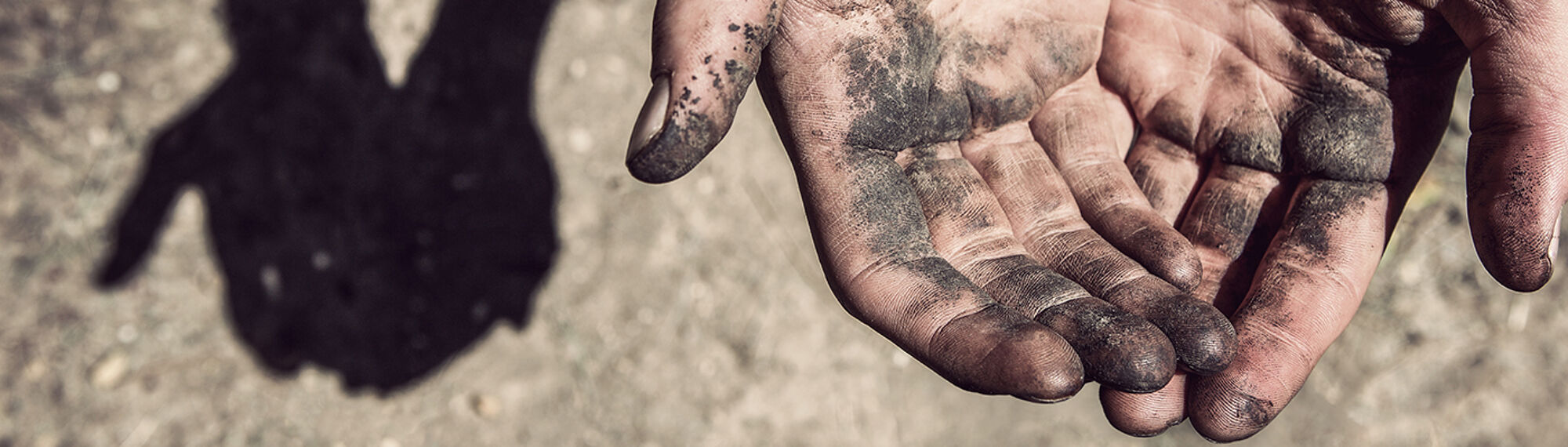 Dirty, working hands. Focus on fingers with shadow on ground